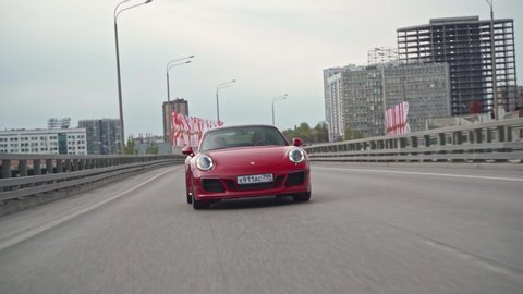 ROSTOV-ON-DON, RUSSIA - APRIL 26, 2020: low angle crane moving rolling shot of a red Porsche 911 Carrera 4S sports car driving on a city at day. Concept of business, traveling, luxury, lifestyle