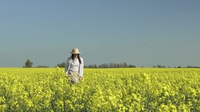 young happy woman, in a straw hat walking in a yellow field and enjoying the sun