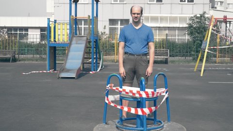 strange bald infantile man stands on an empty enclosed the Playground.