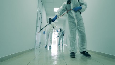 Group of specialists are sanitizing a white hallway