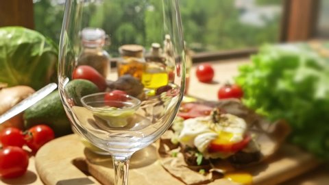 White wine is poured into a glass on the background of a wooden table with vegetables on the balcony.On a table with vegetables,a sommelier pours white Italian wine into a glass on a summer background