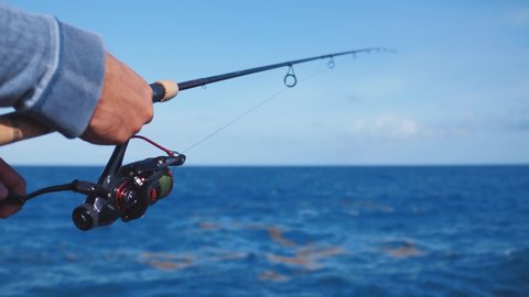 Close-up of a fisherman hands twist reel with fishing line on a rod. Fishing in the blue sea outdoors