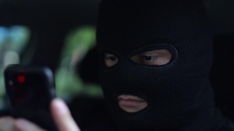 Masked criminal talks on a smartphone, intimidating the victim, extortion, Internet criminals