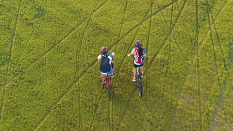Footage B Roll 4k. Aerial view Drone tracking young People riding a bikes on the meadow, aerial view. Love Couple cycling on green lawn together, aerial drone view. Healthy lifestyle concept.