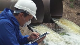 environmental pollution radiation waste concept lifestyle . man chemist scientist in a respirator mask studies water pollution digital tablet and an white helmet stands next to the waste pipes - Powered by Shutterstock - Get 15% off with code: PIKWIZARD15
