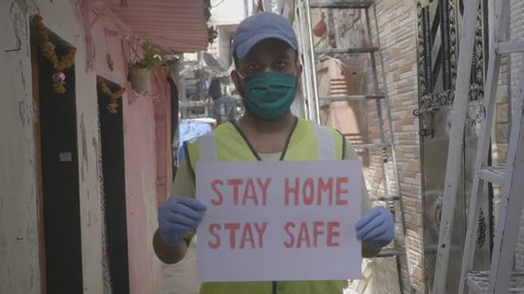 A young man health worker or essential service provider wearing face mask holding a placard with message 'stay home stay safe' during lockdown amid coronavirus or COVID19 epidemic or pandemic 