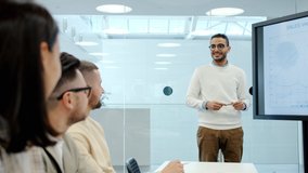 Middle Eastern young man giving lecture about finance in office conference hall talking to group of businesspeople pointing at information on digital screen - Powered by Shutterstock - Get 15% off with code: PIKWIZARD15