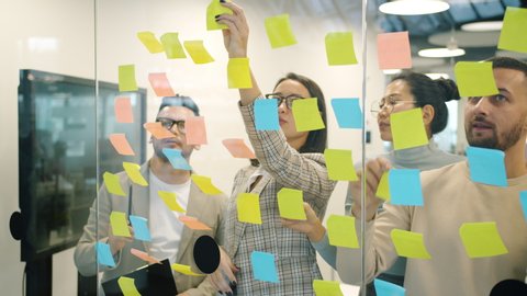 Slow motion of male and female coworkers working with colorful sticky notes brainstorming planning business in office. Meetings and job concept.