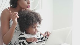 African mother is teaching her daughter to learn multimedia through a laptop during the coronavirus epidemic. Must quarantine at home by teaching them to act in bed in the bedroom. Homeschooling idea 