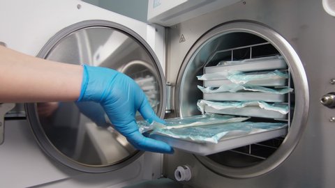 March 8, 2020, Kiev, Ukraine. Dentistry lab. Doctor’s hand puts a bag of dental instruments into a sterilization machine and closes the door. Hygienic processing of high temperature tools before use