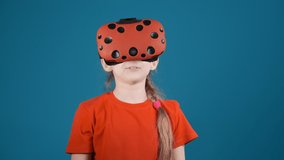 cute little child with long braid takes off virtual reality headset scared by screen picture on blue background slow motion