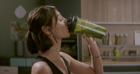 Portrait of fit female drinking green juice detox cocktail in the kitchen at home. Shot with 2x Anamorphic lens