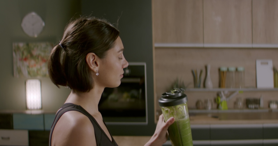Portrait of fit female drinking green juice detox cocktail in the kitchen at home. Shot with 2x Anamorphic lens Royalty-Free Stock Footage #1052980136