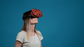 smiling young long haired woman enjoys modern virtual reality headset standing on blue background in studio slow motion