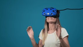 smiling woman plays video game using modern virtual reality headset connected to computer on blue background slow motion