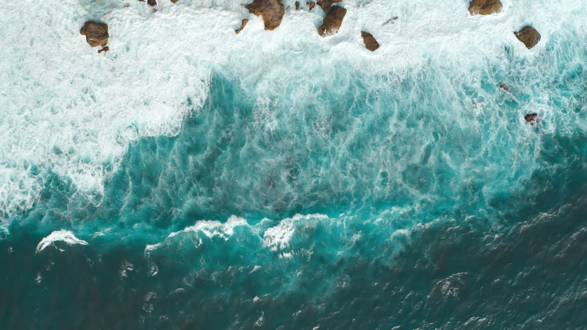 Aerial view from above on a tropical island and ocean waves crashing and foaming against sand beach. Bird's eye aerial shot of golden beach meeting deep blue ocean water. Tourism concept after covid. Royalty-Free Stock Footage #1052981669