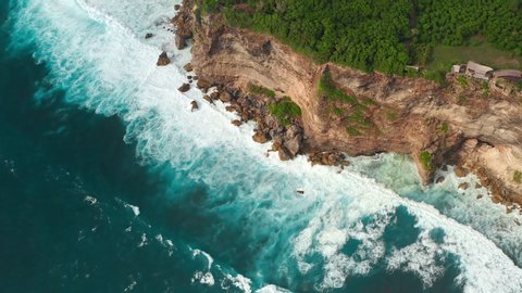 Aerial top view of ocean blue waves break on a beach. Sea waves and beautiful sand beach aerial view drone shot. Bird's eye view of ocean waves crashing against an empty sand beach from above.