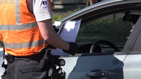DUTCH BELGIAN BORDER – 6 MAY 2020: Belgian police officer wearing gloves checks documents and identity card of driver passing border with the Netherlands, temporary travel restrictions Europe
