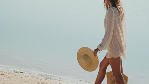 Romantic woman walking on a beach against a beautiful sea bokeh background. Tanned girl in fashionable trendy boho style. Travel vacation, summer outdoor pleasure concept.