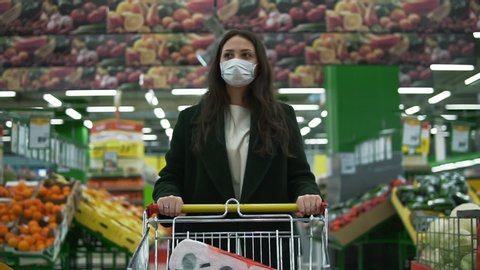 Woman in medical face mask buys basic necessities, hygiene items and food. Girl walks through empty supermarket or grocery store. Quarantine and self-isolation, epidemic covid-19, coronavirus pandemic