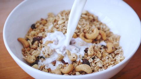 Slow motion milk pouring in bowl of muesli breakfast cereals. Healthy food