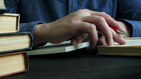 Close-up of hands taking notes in a notebook. A man is studying and reading a book in the library.