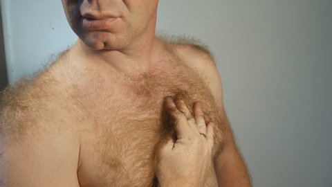 A young man with a naked body strokes the hair on his chest with his hand. A man has a lot of body hair. Hair on the chest, shoulders, stomach. 4K