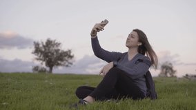 Woman social media influencer using smartphone for vlogging while sitting on grass relaxing in nature