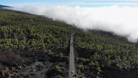 Aerial view of beautiful volcanic landscape with highway and cars driving through the clouds and pine forest. 4K drone footage. Volcano Teide, Tenerife, Canarias. High mountains above cloud level