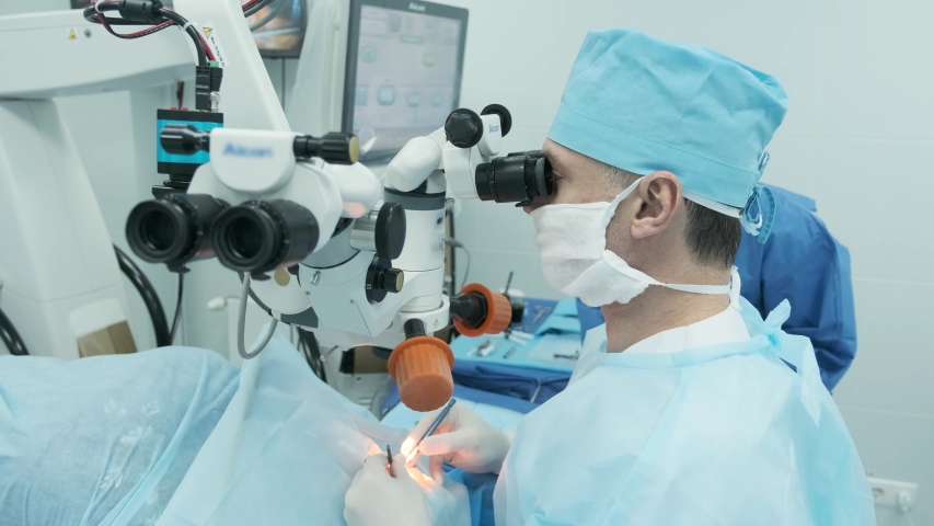 Surgeon looking into the microscope at the eye of female patient at the operating room. Doctor using microscope during eye surgery process, treatment of cataract and diopter correction.