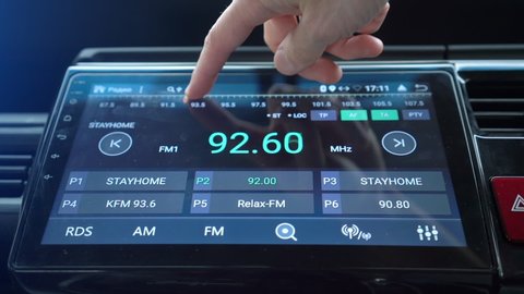 Man finger changing radio stations using smart multimedia touchscreen system for automobile, modern touch screen audio stereo system, transportation and vehicle concept, close up with selective focus