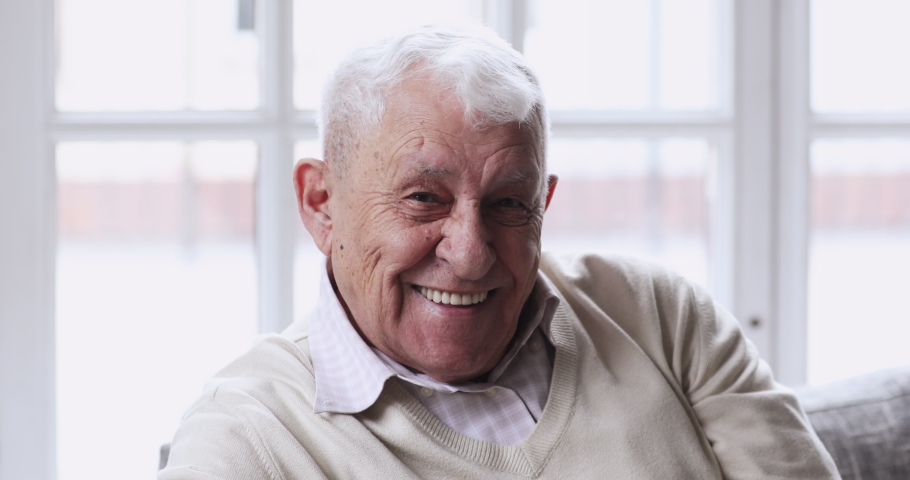 Close up head shot happy middle aged older man with healthy white teeth looking at camera. Portrait of smiling excited elderly mature single grandfather relaxing indoors at home or retirement house. Royalty-Free Stock Footage #1052999630