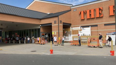 Staten Island, New York / United States - May 15 2020:  Long lines of people wait outside The Home Depot due to Social Distancing rules caused by the Covid-19 pandemic. Camera pans line in front.