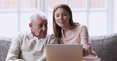 Pretty young woman showing older mature father how to use computer at home. Smiling grownup daughter teaching explaining laptop applications to focused middle age senior dad, modern technology usage.