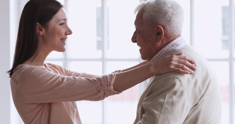 Happy young attractive woman visiting elderly senior father. Excited affectionate middle aged grey haired man greeting loving grownup daughter at home or retirement house, 2 generations reunion.