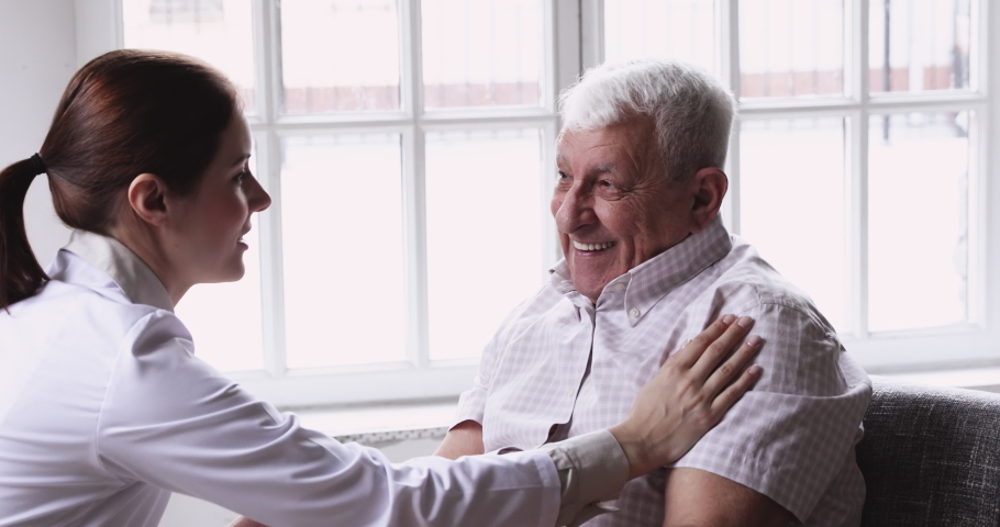 Side view kind young female general practitioner touch shoulder of smiling elderly retired patient, giving healthcare advices or explaining treatment indoors, retirement medical insurance concept. | Shutterstock HD Video #1053004196
