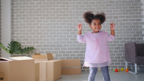 Cute little African American girl dance in living room with boxes or carton and she look fun and happy. Concept of happiness life and stay at home during covid virus pandemic around the world.