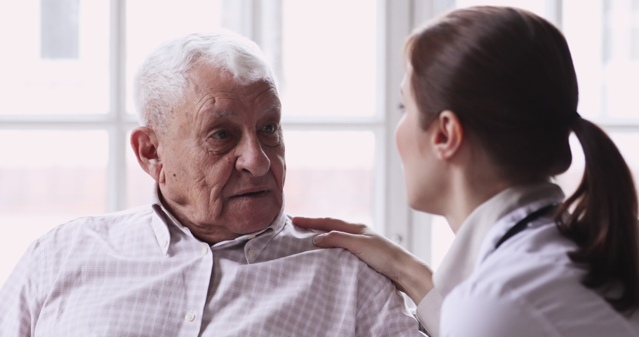 Head shot close up senior old 80s man talking to young nurse in retirement house. Professional general practitioner giving care and support to elderly mature pensioner, consulting about health indoors | Shutterstock HD Video #1053005420