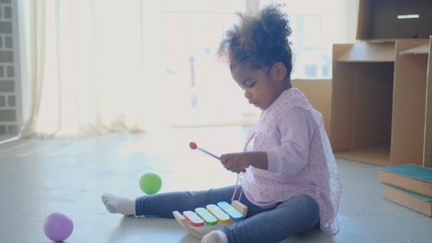 African American girl play with xylophone as toys and she look fun and happy in front of glass window with morning light. Concept of happiness lifestyle for stay at home during covid virus pandemic.
