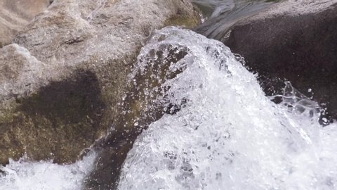 Close up of flowing water splash from mountain river on summer day. Cold spring water flowing bubbly river splash. Stream, nature, rocks.