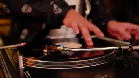 A close-up of the hand of a man who plays on a vinyl record. DJ at work at a party or concert at night.