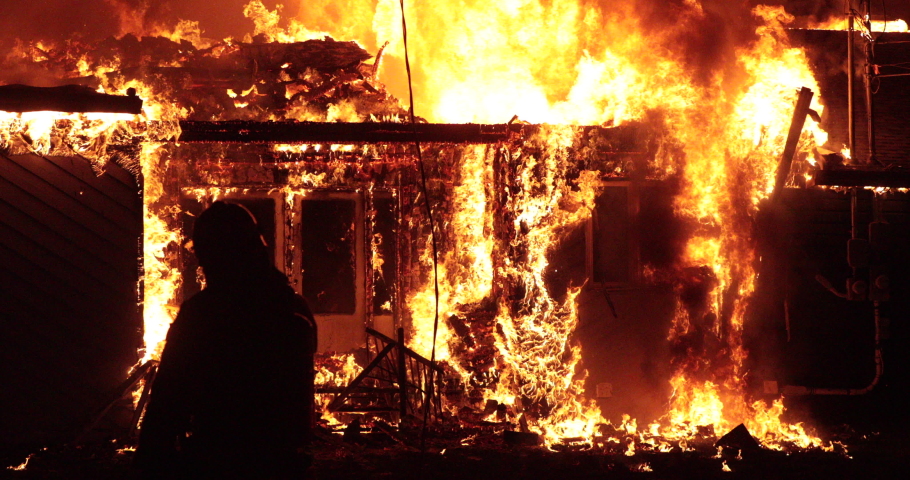 Quebec, Canada - May 2020 - Fully engulfed house fire. Firefighter in shadow in front of fire  