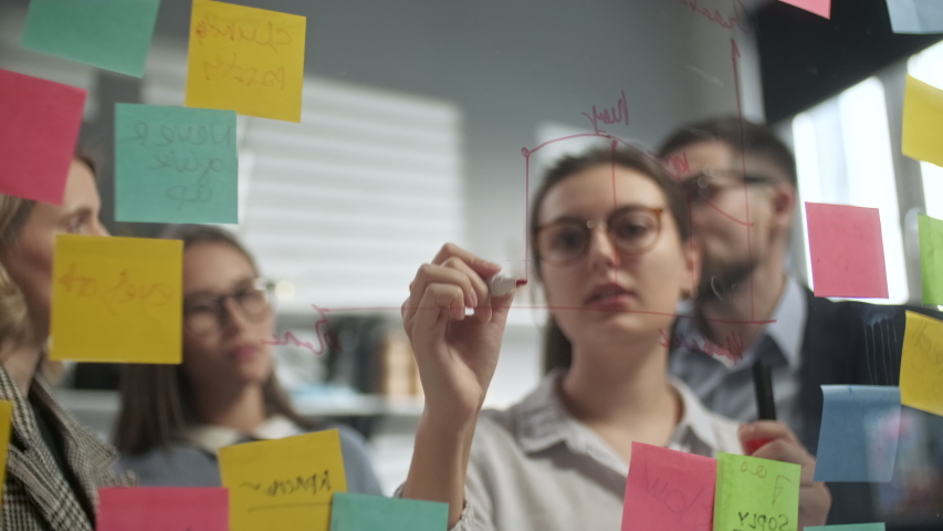 Young Business Team Brainstorming. Business Woman Draws a Graph On Glass Wall With Stickers. Colleagues Approve. Business Success Concept Royalty-Free Stock Footage #1053015077