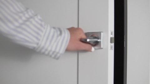Woman's hand closes white door behind doorknob, close-up