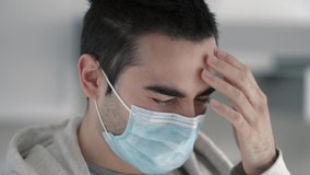 Man suffering from a fever related headache rubbing his forehead while wearing a medical protective face mask