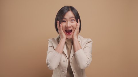 Asian business woman happy smiling and excited looking at camera isolated over beige background. 4K video