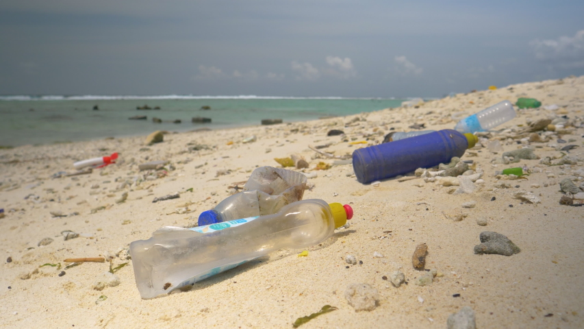 CLOSE UP, DOF: Empty plastic bottles are flooded onto the tropical white sand beach. Sad view of a once pristine tropical coastline filled with garbage. Plastic waste covers the exotic coastline. Royalty-Free Stock Footage #1053033389