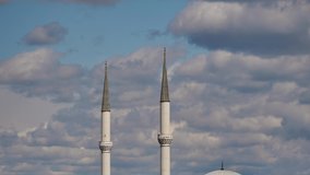 Minarets of a mosque and beautiful clouds passing below blue sky. Sun is shining on minarets when it exits from clouds and making natural lightning effect in timelapse clip
