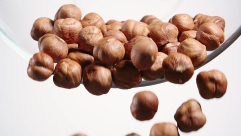 Nuts falling down from the transparent glass bowl on white background. Hazelnut. Slow motion. Close up.