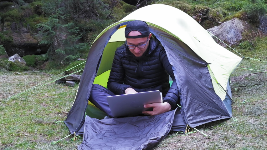 Freelancer or businessman sitting in a tent on nature doing business using a laptop and cellular connection to Internet. Self-isolation during quarantine. Carpathian Mountains, Ukraine. Prores 422. 